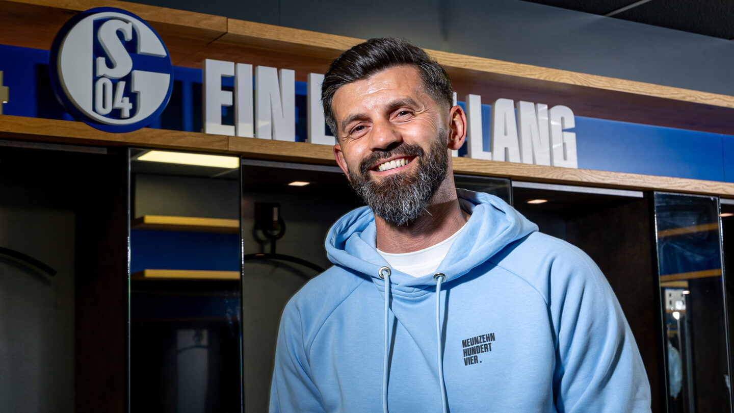 Miron Muslic steht in der Schalke-Kabine vor dem S04-Logo und dem Schriftzug Ein Leben lang