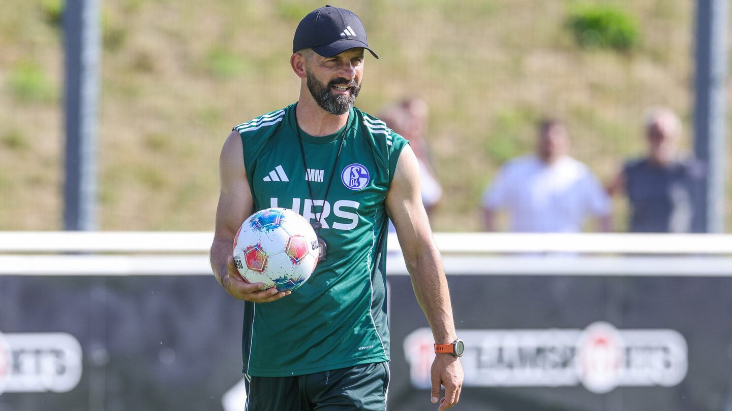 Miron Muslic steht im Trainingsshirt auf dem Trainingsplatz und hält einen Ball in seiner rechten Hand.