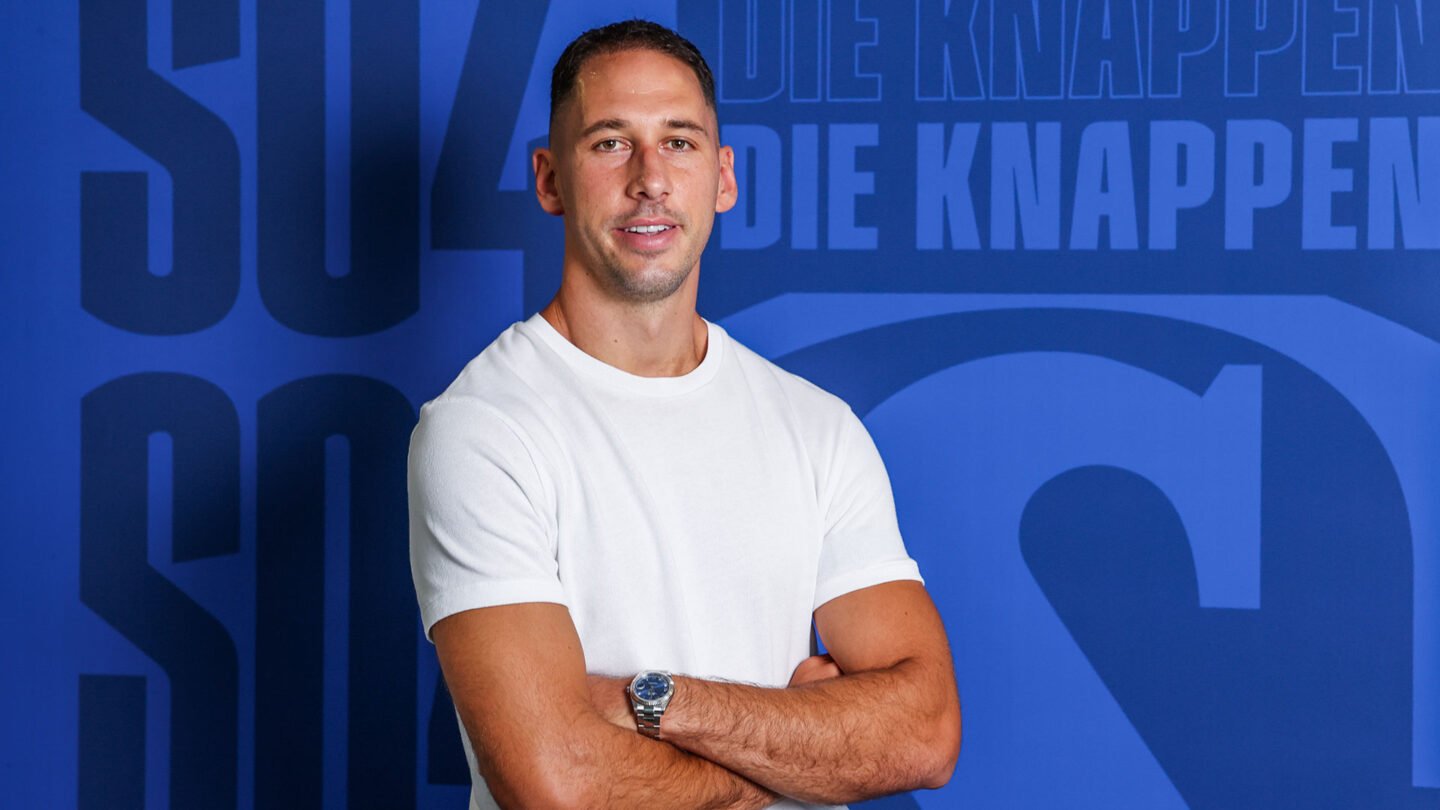Nikola Katic steht vor einer blauen Wand mit den Schriftzügen S04 und die Knappen.