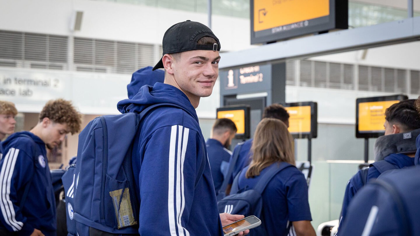 Luca Podlech beim Boarding am Flughafen in München. Im Hintergrund sind mehrere Spieler sowie Bildschirme zu sehen.