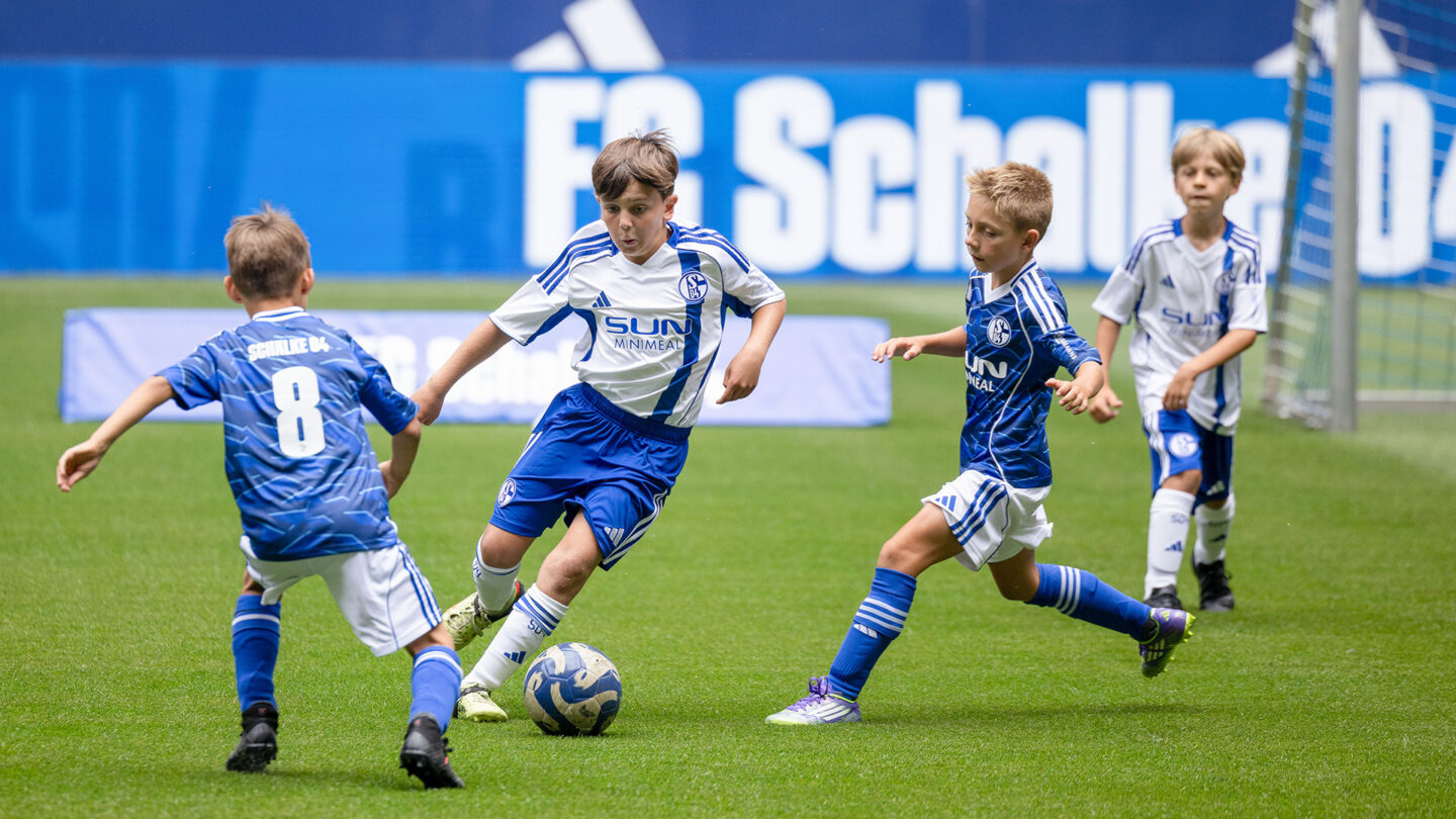 Ein Nachwuchsspieler dribbelt mit dem Ball am Fuß zwei Gegenspieler aus, die von links und rechts heranstürmen.